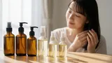 美髪の女性と光が差し込む様々なヘアオイルのボトル
